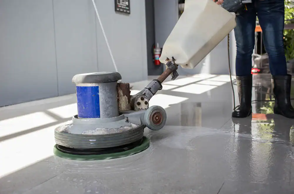 A person using a floor polishing machine, available through equipment rental St. Lucie & Orange County, FL, buffs a shiny, wet floor in a modern indoor space. Only the lower legs and the cleaning equipment are visible.