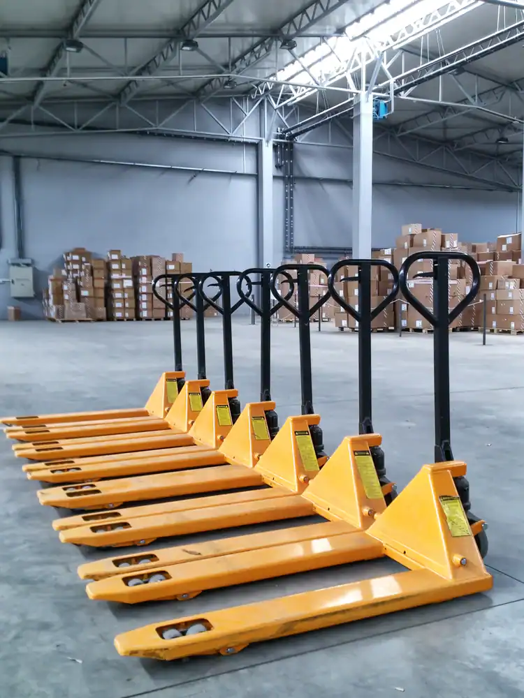 A row of yellow pallet jacks lined up neatly in a spacious FL warehouse, with stacks of cardboard boxes on shelves in the background—ideal for equipment rental St. Lucie & Orange County needs.